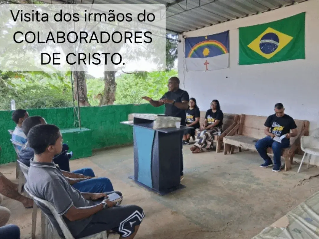 Pregação ao ar livre: um homem fala em pé enquanto outras pessoas ouvem sentadas, sob a cobertura da comunidade.