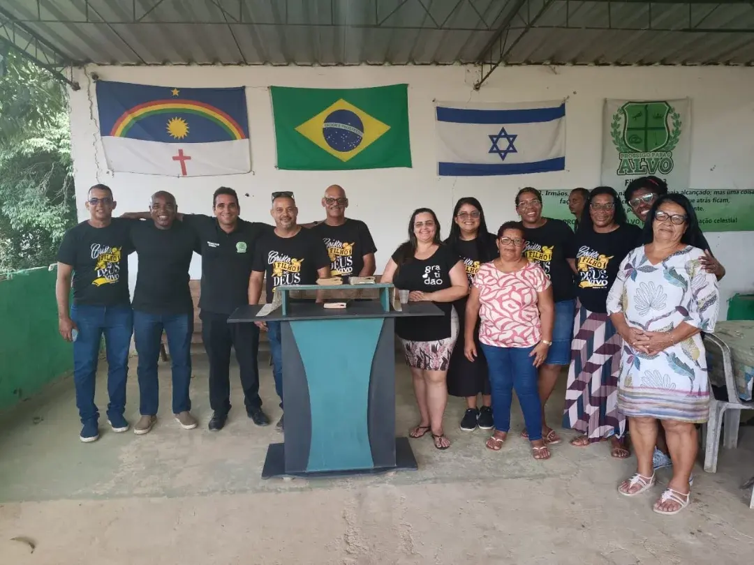 Grupo de colaboradores e voluntários reunidos e sorrindo, com as bandeiras de Pernambuco, do Brasil e de Israel ao fundo.